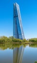 Modern skyscraper reflected in calm water, surrounded by lush greenery under a clear blue sky Royalty Free Stock Photo