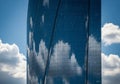 A modern skyscraper with a sleek, curved glass facade reflects the blue sky and white clouds. The Royalty Free Stock Photo