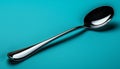 A modern, sleek silver spoon rests on a vibrant teal background