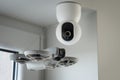 Modern smart home technology concept showing a small white drone hovering near a ceiling mounted security surveillance camera Royalty Free Stock Photo