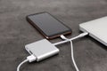 Modern smartphone and laptop charging from power bank on grey table, closeup Royalty Free Stock Photo