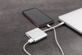 Modern smartphone and laptop charging from power bank on grey table, closeup Royalty Free Stock Photo