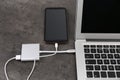 Modern smartphone and laptop charging from power bank on grey table, closeup Royalty Free Stock Photo