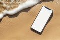 Modern smartphone mockup resting on sandy beach with gentle waves lapping at the shore, showcasing blank screen for creative Royalty Free Stock Photo