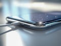 Modern smartphone with sleek curved edges connected to a charging cable resting on a reflective surface in soft natural light Royalty Free Stock Photo