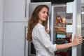 Modern smiling woman standing in the kitchen and open refrigerators door
