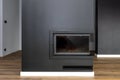 A modern standing fireplace in the living room enclosed with panels, painted black with a corner pane covered with soot.