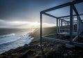 Modern steel frame structure under construction on a rugged coastal cliff overlooking a dramatic ocean at sunset Royalty Free Stock Photo