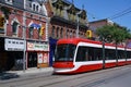 A modern streetcar runs on tracks in front of old Victorian buildings