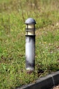 Modern style outdoor lamp with faded black color surrounded with high uncut grass and small flowers