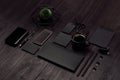 Modern stylish working place with blank black stationery, phone, coffee, green plant on dark wood board, inclined.