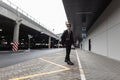 Modern stylish young hipster man in a black leather jacket in jeans in boots in sunglasses walks on the street near the parking Royalty Free Stock Photo