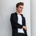 Modern stylish young man in trendy black shirt in a t-shirt with a fashionable hairstyle poses near a white vintage building Royalty Free Stock Photo