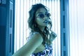 Modern stylish young woman hipster with a fashionable hairstyle in vintage sunglasses in a glamorous swimsuit stands in a solarium Royalty Free Stock Photo