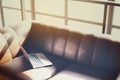 Modern sunny coworking loft office, opened laptop computer on a leather sofa, sunlight through a window