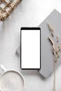 Modern tabletop with with smartphone mockup, cup of coffee, dried plants and notebook on textured white background. Flat lay,