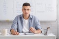 Modern teacher remote and online education concept at home. Attractive man looks at camera, sits at table with notepad