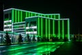 Modern tech building with neon green lines. A bewitching view with reflection of illumination on a wet road