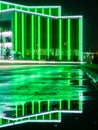 Modern tech building with neon green lines. A bewitching view with reflection of illumination on a wet road Royalty Free Stock Photo