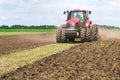 Modern tech red tractor plowing a green agricultural field in spring on the farm. Harvester sowing wheat. Royalty Free Stock Photo