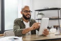 Modern technologies. Happy mature latin man using digital tablet, sitting at desk, browsing internet on modern gadget Royalty Free Stock Photo