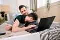 Modern technology. Pretty young gay couple using laptop while posing on bed and spending time together Royalty Free Stock Photo