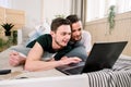 Modern technology. Pretty young gay couple using laptop while posing on bed and spending time together Royalty Free Stock Photo