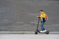 Modern teenager with backpack rides on electric scooter on brick wall background. Boy comes back from school Royalty Free Stock Photo