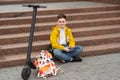 Modern teenager sits on the stairs with mobile phone in hands near his electric scooter. Royalty Free Stock Photo