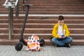 Modern teenager sitting on the stairs near his electric scooter and texting on smartphone. Royalty Free Stock Photo