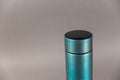 A modern thermos against a gray background. Cylindrical vacuole flask in turquoise color. Container for hot and cold drinks.