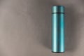 A modern thermos against a gray background. Cylindrical vacuole flask in turquoise color. Container for hot and cold drinks.