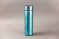 A modern thermos against a gray background. Cylindrical vacuole flask in turquoise color. Container for hot and cold drinks.