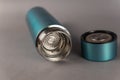 A modern thermos with an open lid lies against a gray background. Cylindrical vacuole flask in turquoise color. Container for hot