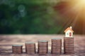 Modern tiny house on stack money coins put to a higher level on the wooden table.