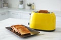 Modern toaster with slices of bread on white marble table in kitchen