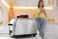 Modern toaster with slices of burnt bread and blurred woman on background