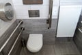 A modern toilet room with a toilet bowl and a toilet paper holder. Metal vandal-proof toilet accessories and handrails for the