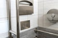 A modern toilet room with a toilet bowl and a toilet paper holder. Metal vandal-proof toilet accessories and handrails for the