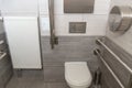 A modern toilet room with a toilet bowl and a toilet paper holder. Metal vandal-proof toiletries and handrails for the disabled
