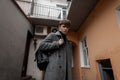 Modern trendy young man model walks with a leather black stylish backpack in a gray checkered coat around the city. Handsome cool Royalty Free Stock Photo