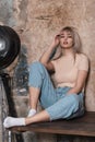 Modern trendy young woman blonde in stylish casual clothes posing near a vintage black metal lamp indoors with a old brick wall. Royalty Free Stock Photo