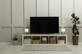 Modern TV on cabinet, lamps and houseplants near white wall in room. Interior design Royalty Free Stock Photo