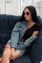 Modern urban young hipster woman in fashionable sunglasses in a trendy black T-shirt in a stylish denim jacket in a skirt Royalty Free Stock Photo