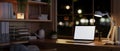A modern, vintage, and cozy home office workspace at night with a white-screen laptop mockup Royalty Free Stock Photo