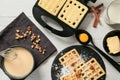Modern waffle maker with dough and ingredients on light wooden table Royalty Free Stock Photo