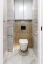 Modern wall-mounted white toilet bowl, black button the background of a beige bathroom wall. Part of the interior of the