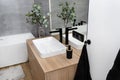 A modern washbasin in the bathroom in a wall-mounted cabinet with a matte black faucet, a visible mirror and artificial flowers. Royalty Free Stock Photo