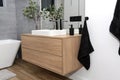 A modern washbasin in the bathroom in a wall-mounted cabinet with a matte black faucet, a visible mirror and artificial flowers. Royalty Free Stock Photo