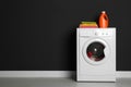 Modern washing machine with laundry, stack of towels and detergent near black wall. Space for text Royalty Free Stock Photo